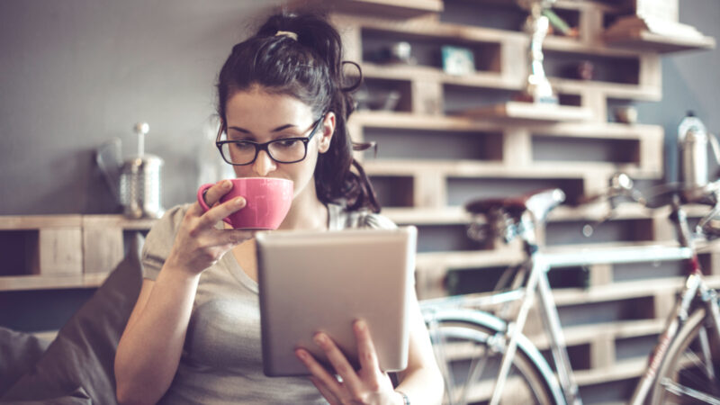 eine junge Frau mit Brille trinkt Kaffee und liest auf ihrem Tablet